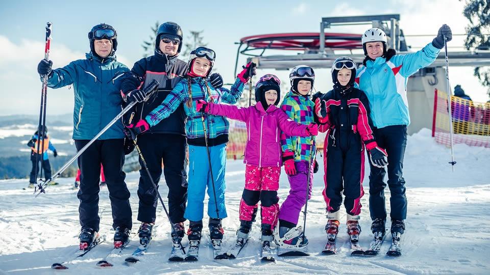 Skiareal Lipno - rodina stojící na sjezdovce ve Skiareálu Lipno v pozadí s lanovkou.